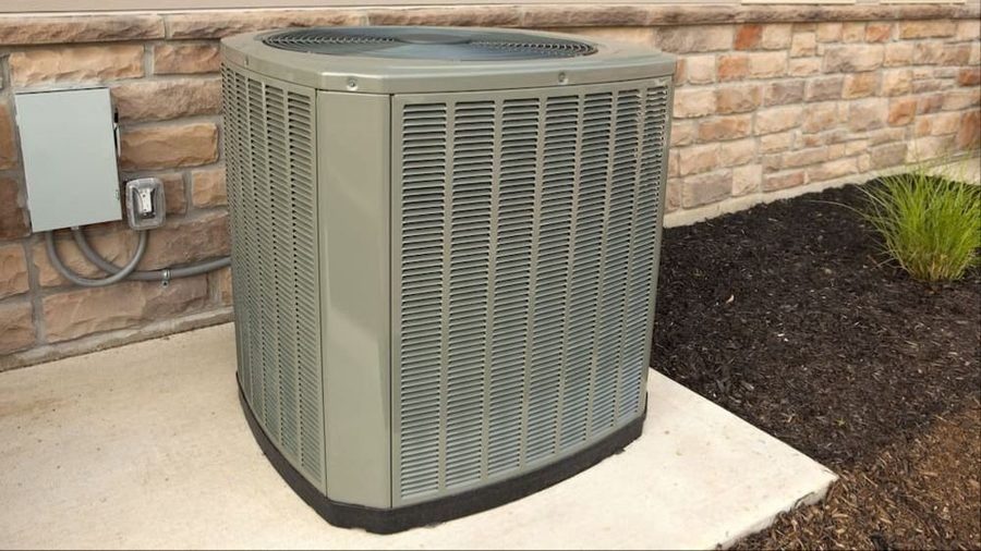 Outdoor air conditioner condenser unit on a concrete pad beside a brick wall.